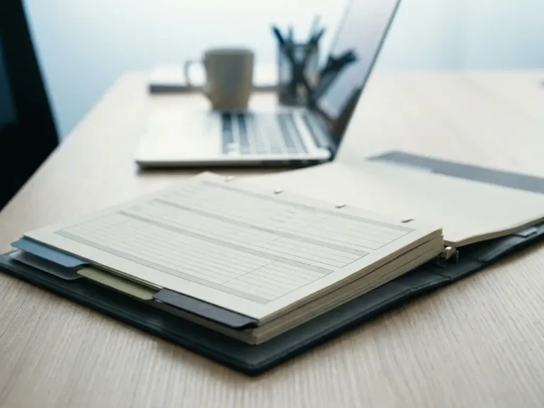 Geöffneter Compliance-Ordner mit farbigen Registerreitern auf modernem Schreibtisch, Laptop im Hintergrund, professionelle IT-Büroumgebung.